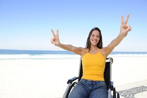 happy disabled woman in wheelchair outdoors beach showing victory sign